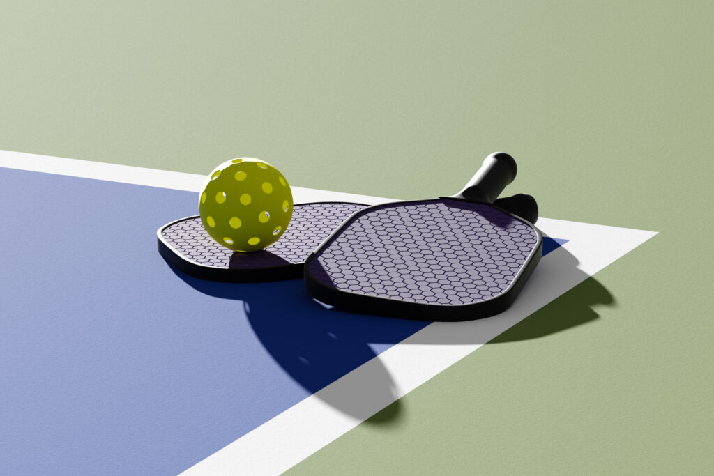 A Pickleball paddles and ball on the court.