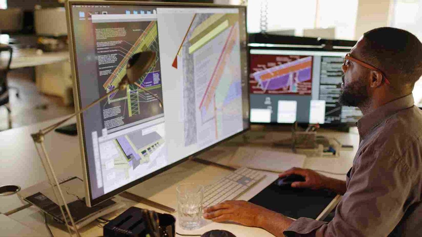 Man with dual monitors researches sustainable building material benefits in Oklahoma City